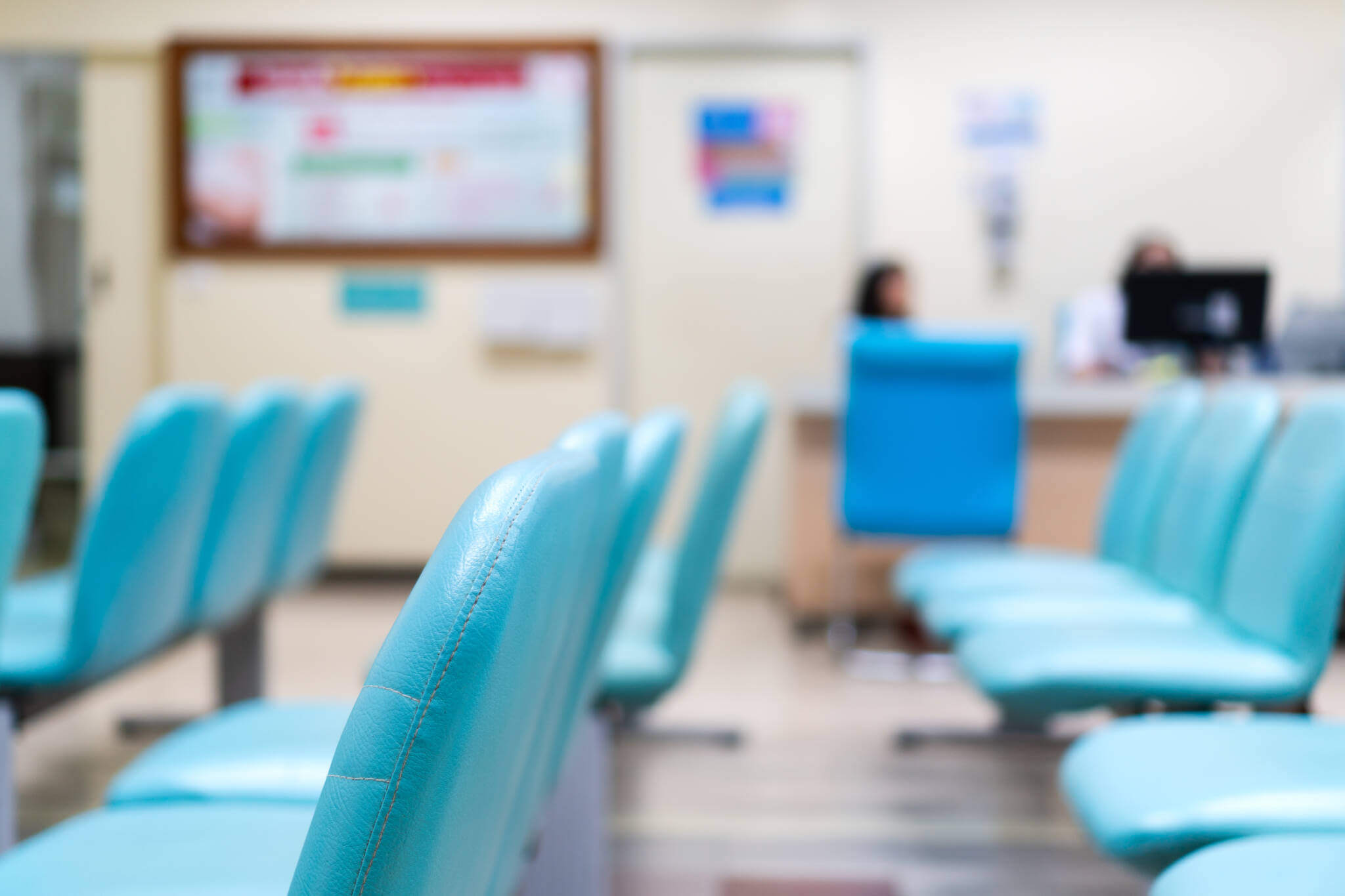 Empty Blue Chair In Waiting Room At Hospital With Blurred Background Of Nurse Desk.
