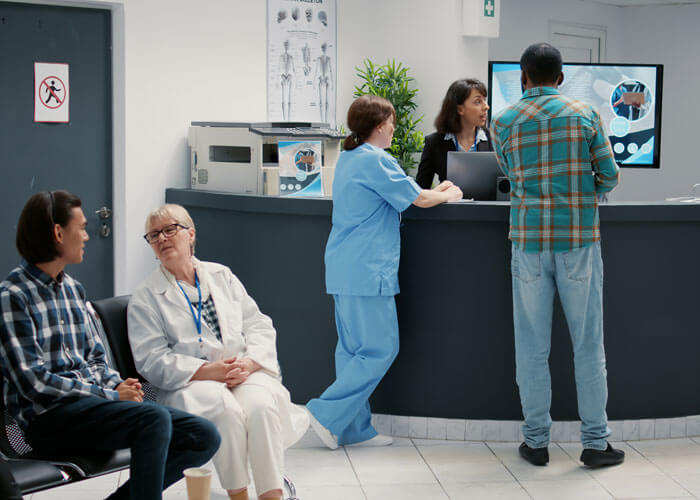 Diverse Group Of Patients Sitting In Waiting Room Area To Register For Appointment